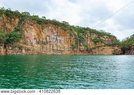Rock Walls With Orange Tones Next To The Lake And Green Vegetation Growing On Rocks Of The Canyons O