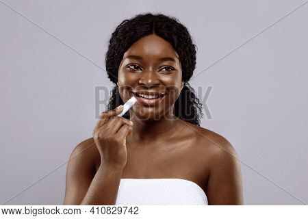 Pretty Black Female Holding Chapstick, Applying Lip Balm Over Gray Studio Background, Young African 