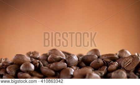 Falling Roasted Coffee Beans on Brown Background, close-up.