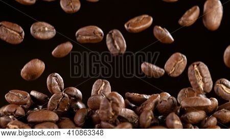 Falling Roasted Coffee Beans on Black Background, close-up.