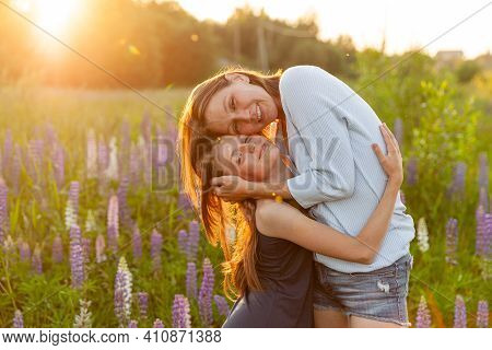Young Mother Embracing Her Child Outdoor. Woman And Teenage Girl On Summer Field With Blooming Wild 