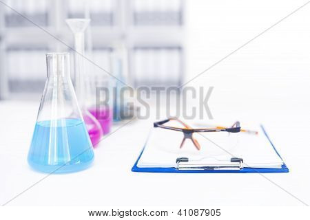 Chemical Flasks With Reagents And Clipboard Isolated Over White Background
