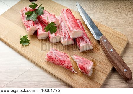 Appetizing crab sticks on wooden cutting board is laying on light table. Selective focus on cut crab stick