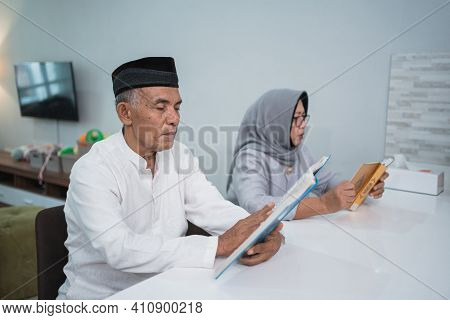 Asian Muslim Senior Man Teaching Wife Reading Koran Or Quran In Living Room