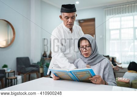 Asian Muslim Senior Man Teaching Wife Reading Koran Or Quran In Living Room