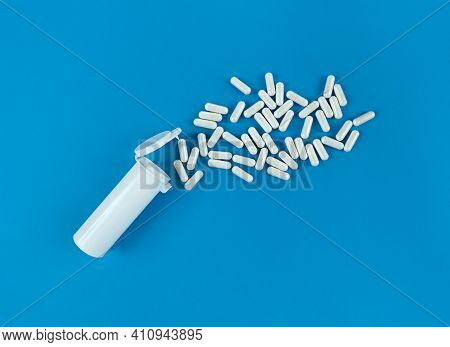 White Plastik Medical Bottle And Scattered Pills Capsules On A Blue Backdrop With Copy Space.