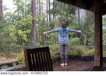 Woman Spread Her Arms To The Sides And Enjoys The Warm Rain, Standing On The Veranda And Looking At 