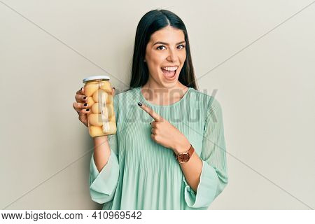 Young hispanic woman holding bottle with boiled potatoes smiling happy pointing with hand and finger 