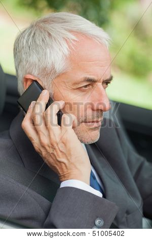 Serious businessman on the phone driving cabriolet on sunny day