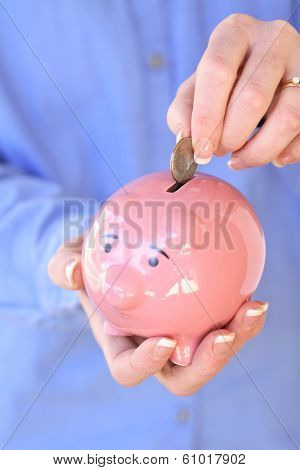 Woman in blie shirt holding pink pig bank and placing coin inside 