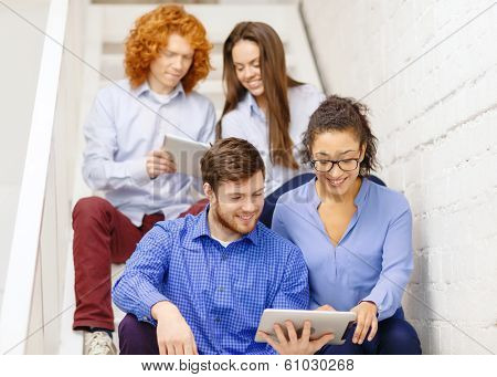 business, technology and startup concept - smiling creative team with tablet pc computer sitting on staircase