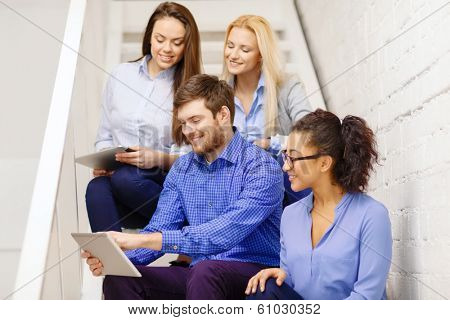 business, technology and startup concept - smiling creative team with tablet pc computer sitting on staircase
