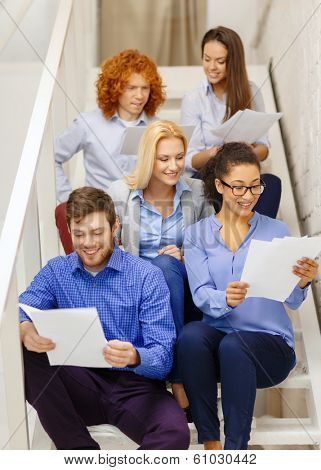business, office and startup concept - smiling creative team with papers and take away coffee on staircase