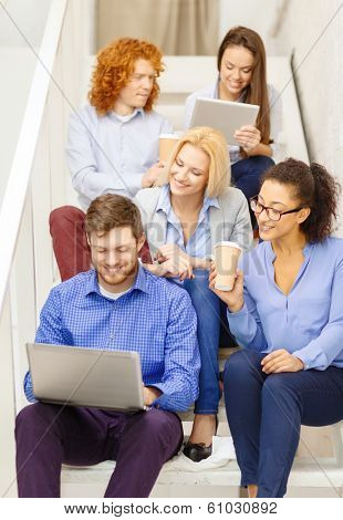 business, technology and startup concept - smiling creative team with laptop and tablet pc computer sitting on staircase
