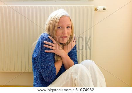 a young woman sits in front of a radiator in winter. room temperature is too low.