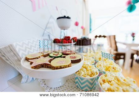 Berries, popcorn, canapes, candies, chocolate cake pops and a cake on a dessert table at party