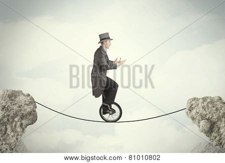 Brave business man riding an mono cycle between cliffs concept