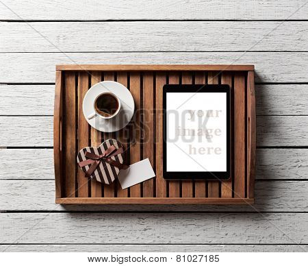 Gift box with blank tag, cup of coffee and digital tablet pc on salver on white wood table.