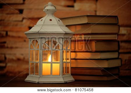 Books and decorative lantern on table and brick wall background