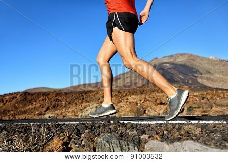 Running athlete man runner jogging on nature road in forest mountain. Lower half body running shoes and legs of male adult on a jog in summer.
