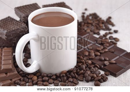 White Cup Of Hot Chocolate On Coffee Beans And Chocolate Background