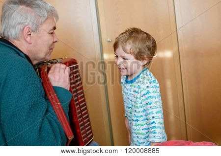Little kid boy and grandfather playing music instrument