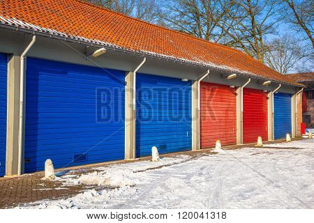Garage Doors In In Blue And Red Next To Each Other On A Snowy Winter Day