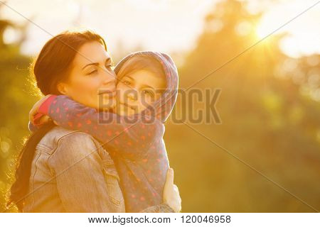 Portrait of beautiful mother with love hugging her precious daughter in bright yellow sunlight in the park, happy family life