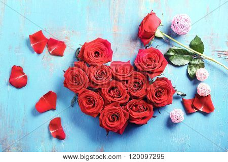 Fresh red roses buds in shape of heart on blue wooden background