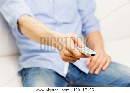 home, people, technology and entertainment concept - close up of man changing channels with tv remote control at home