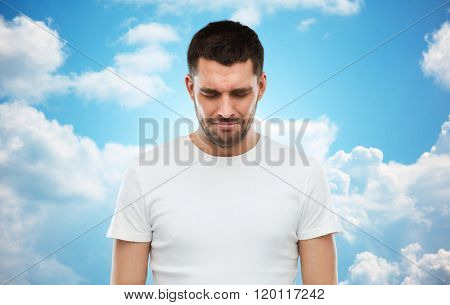 emotion, sadness and people concept - unhappy young man over blue sky and clouds background