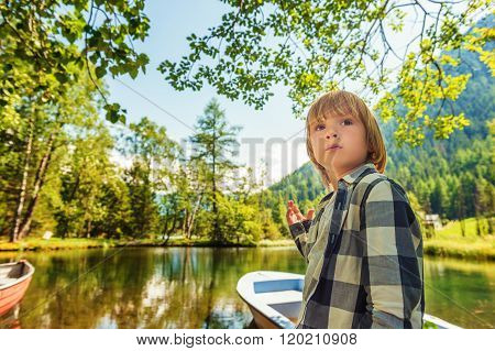 Cute little boy hiking in swiss Alps, resting by the lake