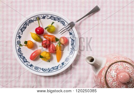 Sweet Dessert In Fruit Shape On Dish With Small Fork And Tea Pot On Pink Tablemat Background