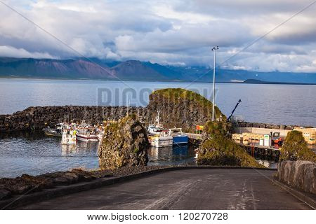 Sunset on the sea fjord in Iceland. White fishing boat in the harbor pier fishing village Arnastapi
