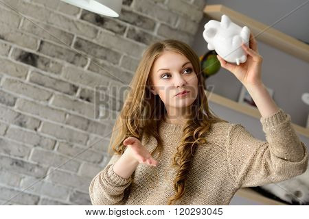 Young blond woman trying to find more money in the piggy bank lifting it over his head