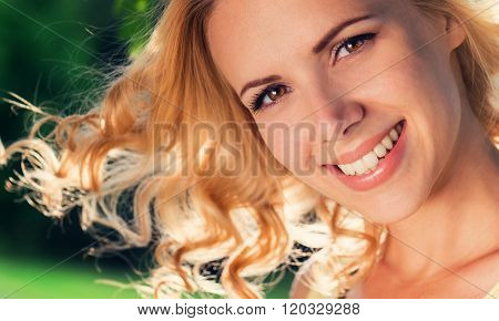Blond woman, flipping curly hair. Sunny summer nature.