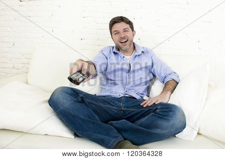young happy man watching tv lying at home living room sofa with remote control looking relaxed smiling and laughing enjoying television program comedy movie or sitcom