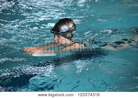 Close up of child practicing flutter kick with kick board in  indoor swimming pool