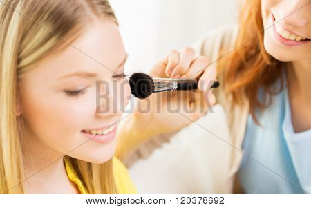beauty, make up, cosmetics and people concept - close up of smiling young woman and visagist or friend with blush and makeup brush