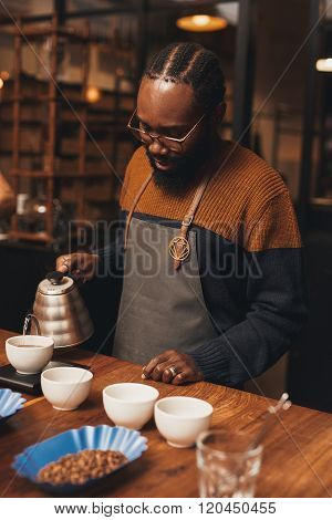 African barista pouring coffee in a modern roastery