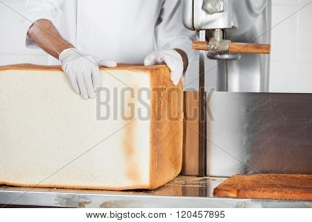 Baker Holding Big Bread Loaf At Cutting Machine In Bakery