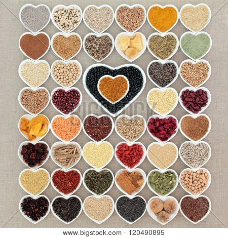 Large dried superfood collection in heart shaped porcelain bowls forming an abstract background over hessian background. High in minerals, vitamins and antioxidants.