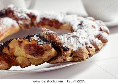 closeup of a spanish O-shaped mille-feuille cake filled with chocolate and topped with icing sugar and chocolate sprinkles