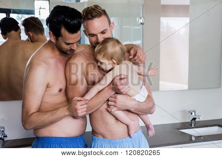 Happy gay couple holding their child in bathroom