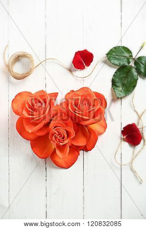 Fresh red roses buds in shape of heart with rope and scissors on wooden background