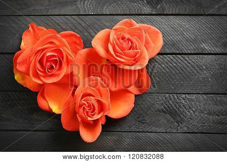 Fresh red roses buds in shape of heart on wooden background
