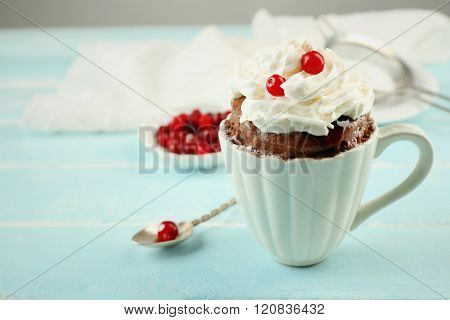 Mug cake with cream and cranberry on blue wooden background