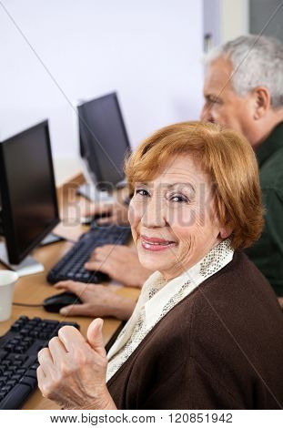 Happy Senior Woman Gesturing Thumbsup At Desk In Computer Class