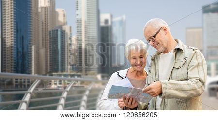 family, age, tourism, travel and people concept - happy senior couple with map and city guide on street over dubai city waterfront background