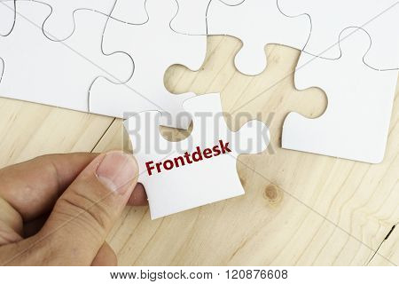 Hand holding piece of jigsaw puzzle on wooden surface